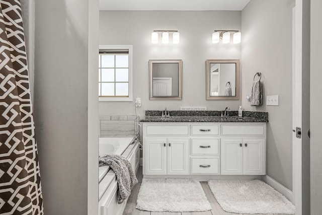 bathroom featuring double vanity, a garden tub, baseboards, and a sink