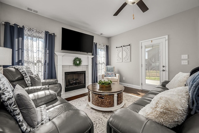 living room featuring baseboards, visible vents, a ceiling fan, light wood-style flooring, and a fireplace