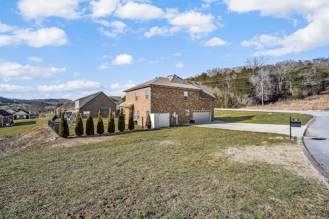 view of side of property with a lawn, concrete driveway, an attached garage, fence, and brick siding