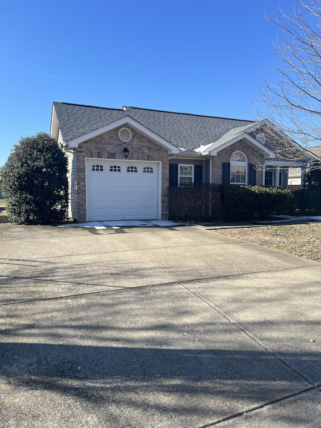 single story home featuring a garage, concrete driveway, brick siding, and roof with shingles