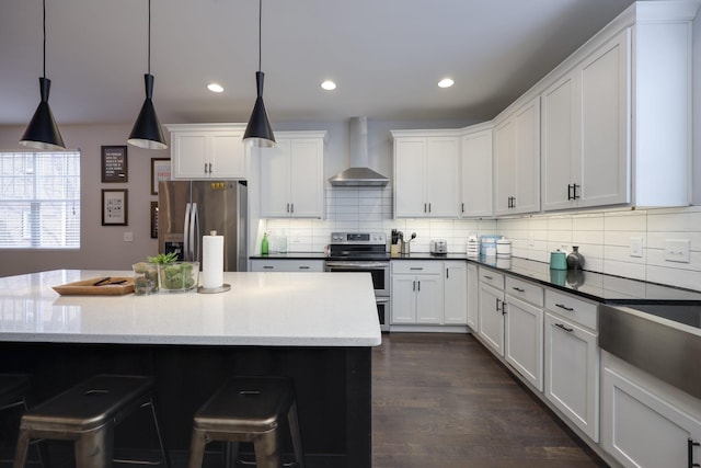 kitchen with decorative light fixtures, backsplash, appliances with stainless steel finishes, white cabinetry, and wall chimney range hood