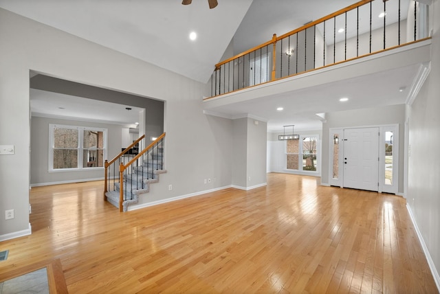 unfurnished living room with light wood-type flooring, baseboards, stairs, and high vaulted ceiling