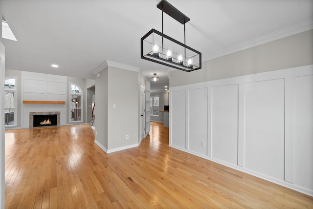 unfurnished living room with a decorative wall, a lit fireplace, ornamental molding, light wood finished floors, and plenty of natural light