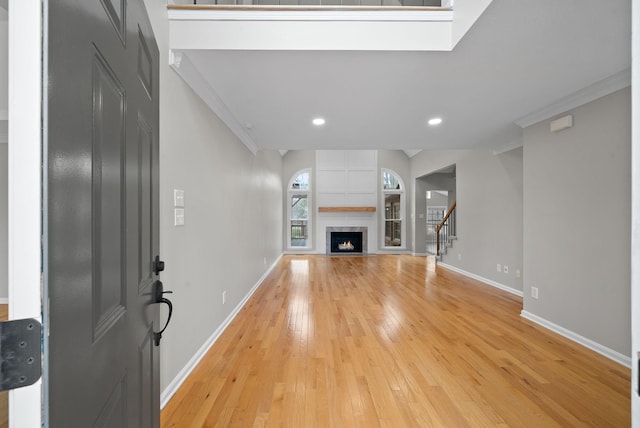 unfurnished living room featuring light wood-type flooring, stairs, baseboards, and ornamental molding