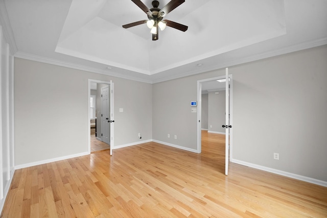 unfurnished bedroom featuring light wood finished floors, baseboards, a ceiling fan, ornamental molding, and a tray ceiling