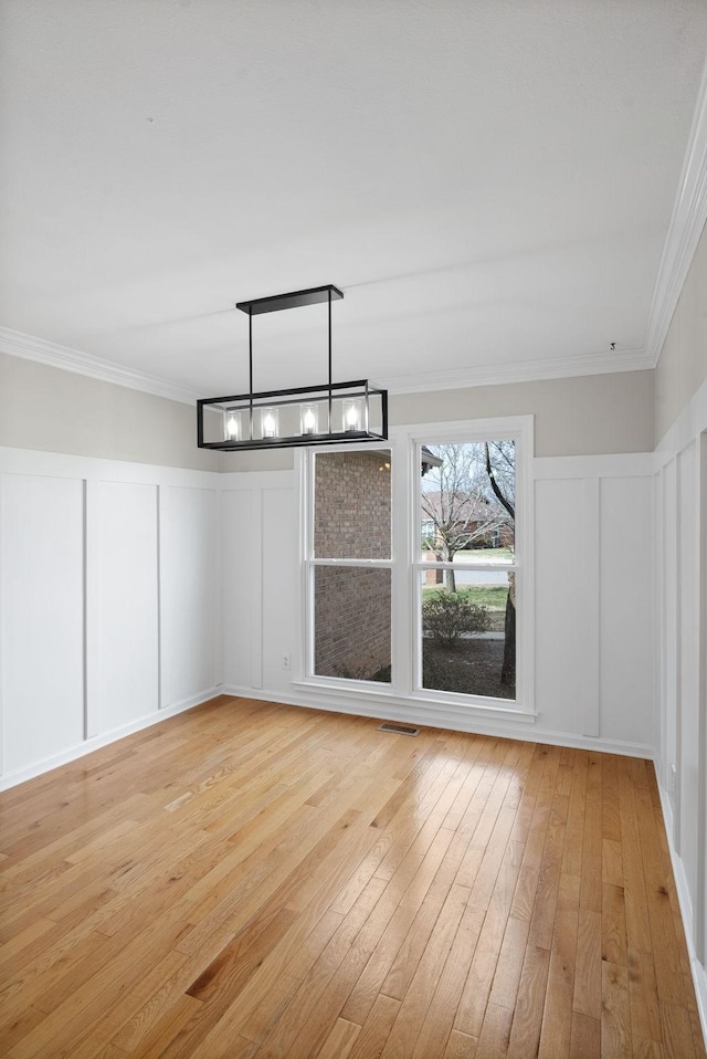 empty room with a decorative wall, visible vents, light wood-type flooring, an inviting chandelier, and crown molding