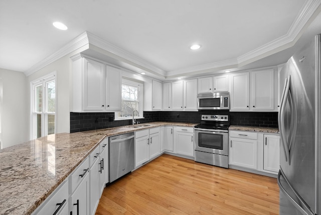 kitchen with white cabinets, appliances with stainless steel finishes, light stone counters, light wood-style floors, and a sink