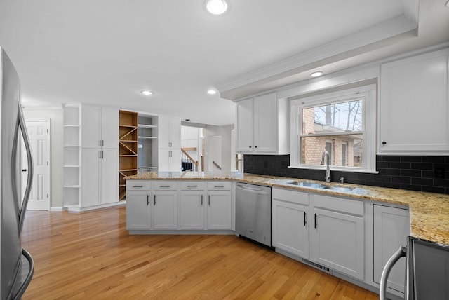 kitchen with light wood finished floors, appliances with stainless steel finishes, white cabinets, a sink, and a peninsula