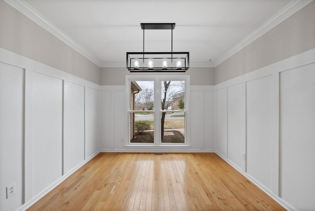 unfurnished dining area with crown molding, an inviting chandelier, light wood-style flooring, and a decorative wall