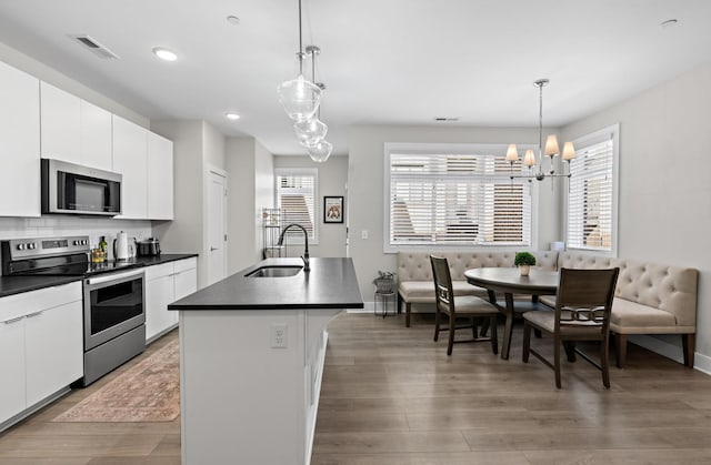 kitchen featuring stainless steel appliances, a sink, hanging light fixtures, dark countertops, and a center island with sink