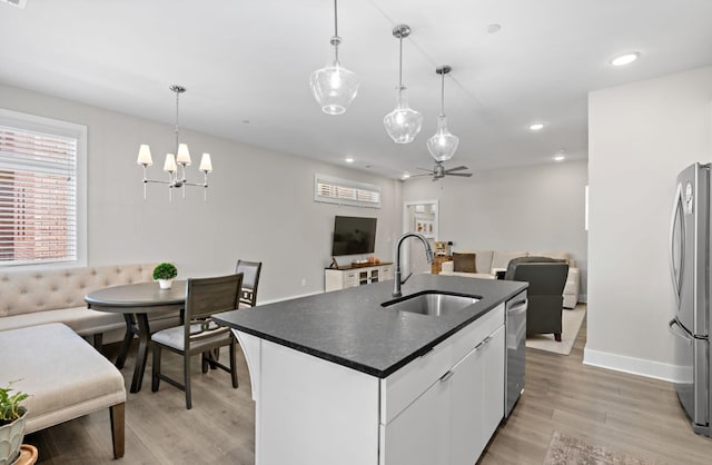 kitchen with pendant lighting, dark countertops, white cabinetry, a sink, and a kitchen island with sink