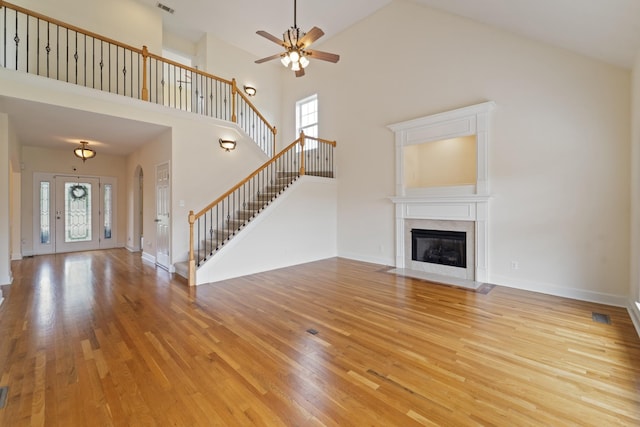 unfurnished living room with light wood-type flooring, a fireplace with flush hearth, stairs, and baseboards