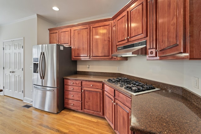 kitchen with light wood-style flooring, dark stone countertops, stainless steel appliances, crown molding, and under cabinet range hood