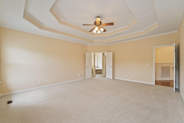 empty room featuring ornamental molding, a tray ceiling, visible vents, and light carpet