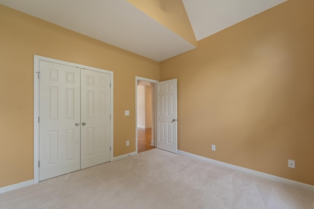 unfurnished bedroom with a closet, light colored carpet, and baseboards