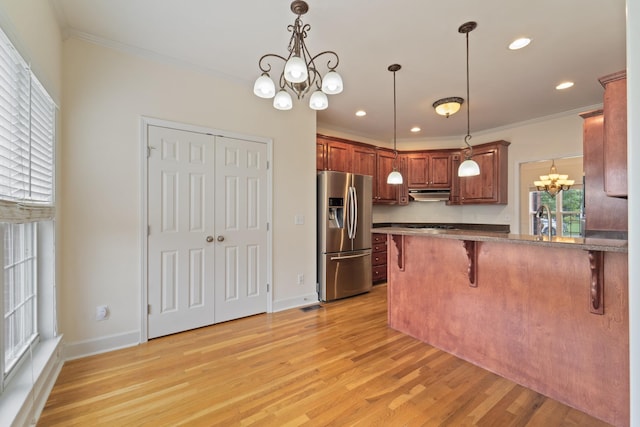 kitchen with a breakfast bar area, under cabinet range hood, a peninsula, stainless steel refrigerator with ice dispenser, and dark countertops