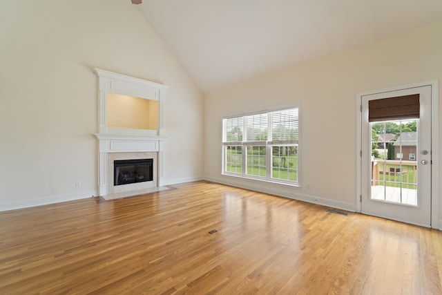 unfurnished living room with light wood finished floors, visible vents, a fireplace with flush hearth, high vaulted ceiling, and baseboards