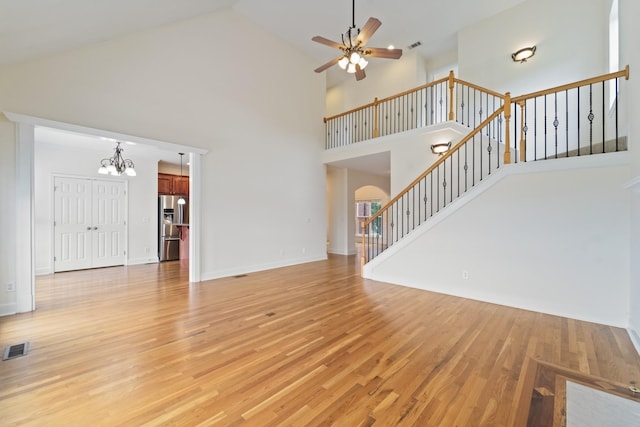 unfurnished living room with light wood-type flooring, stairs, visible vents, and ceiling fan with notable chandelier