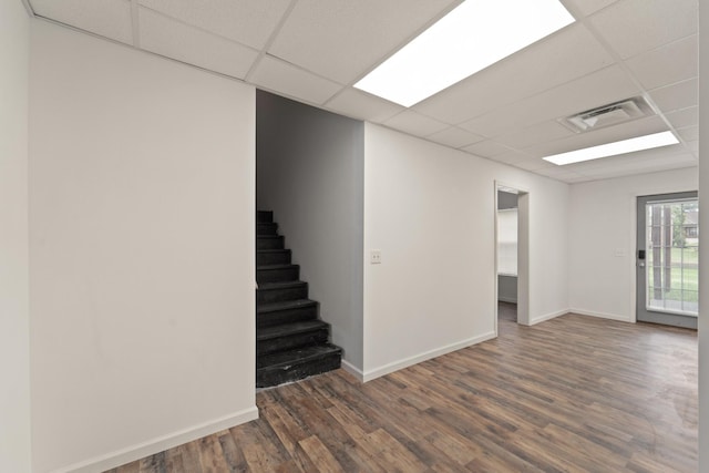 basement featuring baseboards, visible vents, dark wood finished floors, stairway, and a paneled ceiling