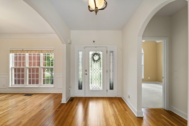 entrance foyer featuring arched walkways, light wood-style flooring, a decorative wall, a wainscoted wall, and visible vents