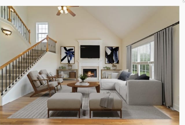 living area featuring high vaulted ceiling, a warm lit fireplace, stairway, and light wood finished floors