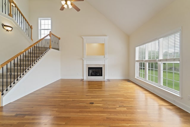 unfurnished living room with stairway, light wood-style floors, a fireplace with flush hearth, high vaulted ceiling, and baseboards