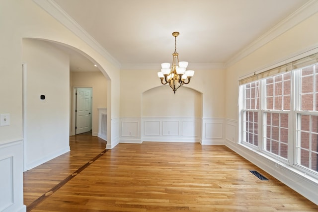 unfurnished dining area with arched walkways, light wood-style flooring, visible vents, ornamental molding, and an inviting chandelier