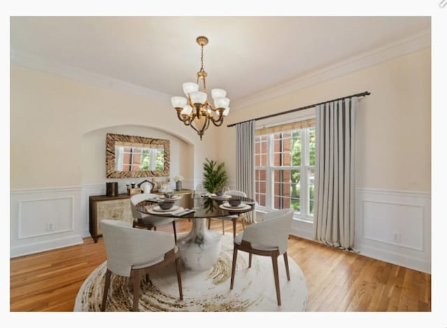 dining space featuring a chandelier, wainscoting, wood finished floors, and crown molding