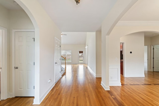 hall featuring light wood finished floors, stairway, baseboards, and arched walkways