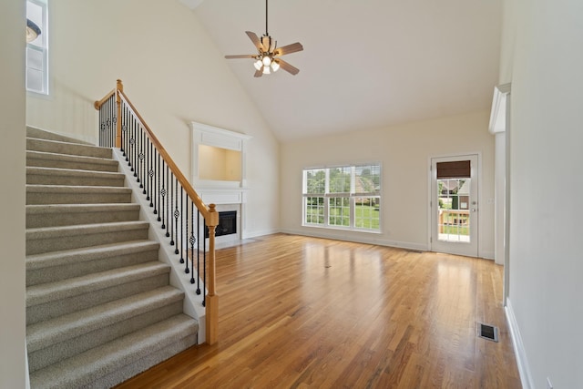 unfurnished living room featuring light wood finished floors, visible vents, a fireplace with flush hearth, high vaulted ceiling, and stairs