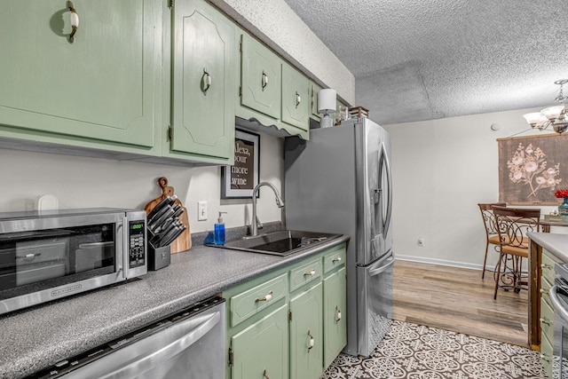 kitchen with a textured ceiling, a chandelier, a sink, green cabinets, and appliances with stainless steel finishes