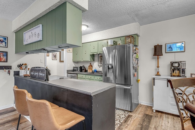 kitchen with a textured ceiling, light wood-style flooring, a peninsula, green cabinets, and appliances with stainless steel finishes