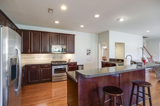 kitchen with decorative backsplash, a breakfast bar, stainless steel appliances, light wood-type flooring, and a sink