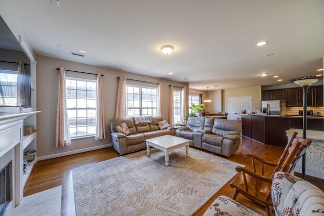 living area with light wood finished floors, recessed lighting, visible vents, a fireplace with flush hearth, and baseboards