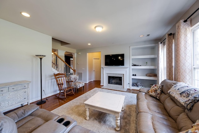 living room with built in features, visible vents, a premium fireplace, stairway, and wood finished floors