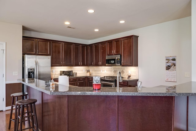 kitchen with a breakfast bar area, tasteful backsplash, recessed lighting, appliances with stainless steel finishes, and dark brown cabinetry