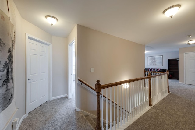 hallway featuring carpet floors, an upstairs landing, and baseboards