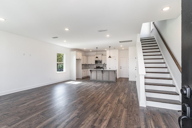 unfurnished living room featuring baseboards, stairway, dark wood-style flooring, a sink, and recessed lighting