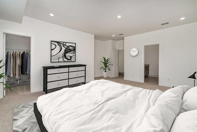 bedroom featuring a walk in closet, recessed lighting, light colored carpet, visible vents, and baseboards