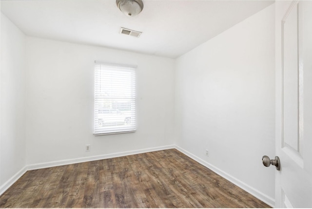 empty room with dark wood-type flooring, visible vents, and baseboards