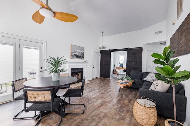 dining room featuring high vaulted ceiling, a barn door, wood finished floors, visible vents, and a ceiling fan