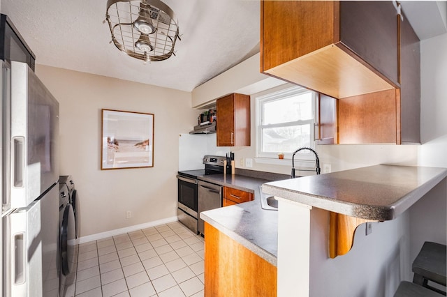 kitchen with dark countertops, brown cabinets, stainless steel appliances, a kitchen bar, and a sink