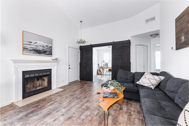 living room featuring high vaulted ceiling, a barn door, wood finished floors, and visible vents