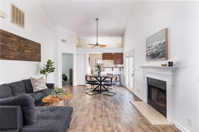 living room featuring high vaulted ceiling, a fireplace, visible vents, and wood finished floors