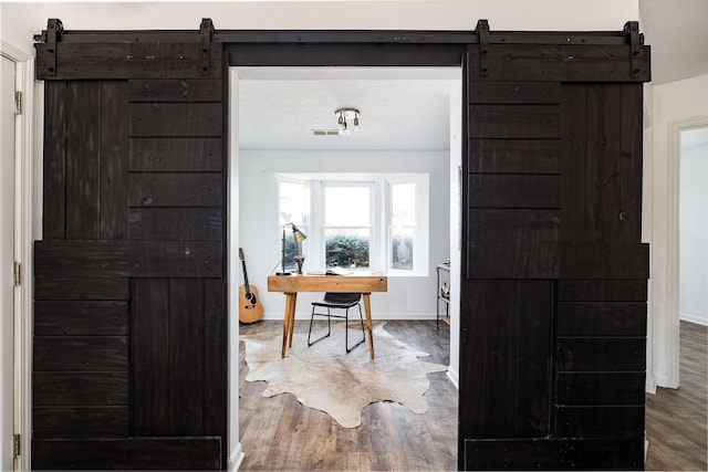 interior space featuring baseboards, a barn door, visible vents, and wood finished floors