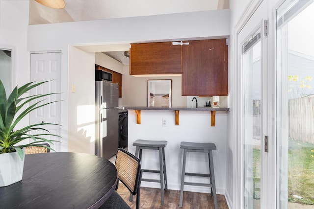 kitchen with dark wood finished floors, freestanding refrigerator, a peninsula, a kitchen bar, and black microwave