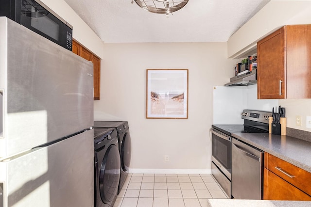 kitchen featuring under cabinet range hood, separate washer and dryer, appliances with stainless steel finishes, brown cabinetry, and dark countertops