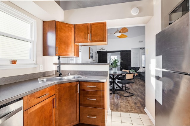 kitchen featuring a ceiling fan, dark countertops, brown cabinets, stainless steel appliances, and a sink