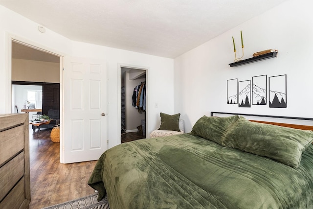 bedroom with a barn door, a walk in closet, and dark wood-style flooring