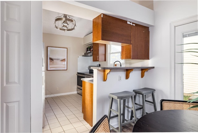 kitchen featuring electric range, baseboards, a breakfast bar area, a peninsula, and light tile patterned flooring